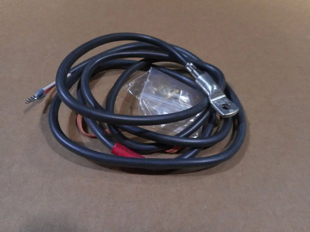 Kabel mit einem angeschlossenen Metallring und zwei abisolierten Leitungen. Verpackung mit kleinen Metallteilen im Hintergrund. Produkt von Remeha.